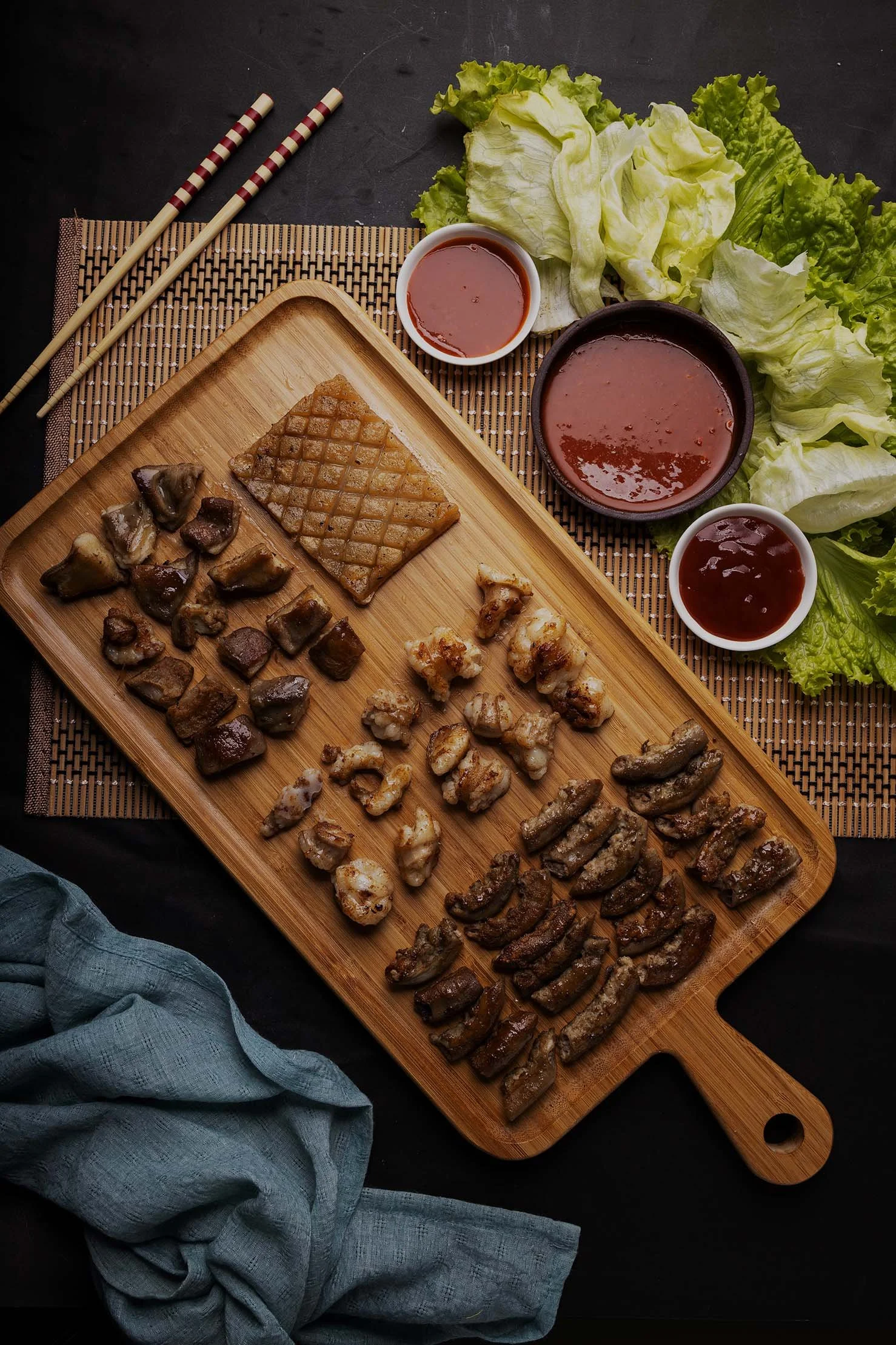 A wooden serving board filled with perfectly grilled, premium Korean BBQ meats, accompanied by dipping sauces and fresh lettuce wraps at Korea BBQ & Sushi in Brentwood, TN.