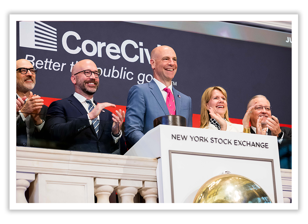 Group of people standing behind a podium at the New York Stock Exchange, with a large screen displaying the CoreCit logo in the background.
