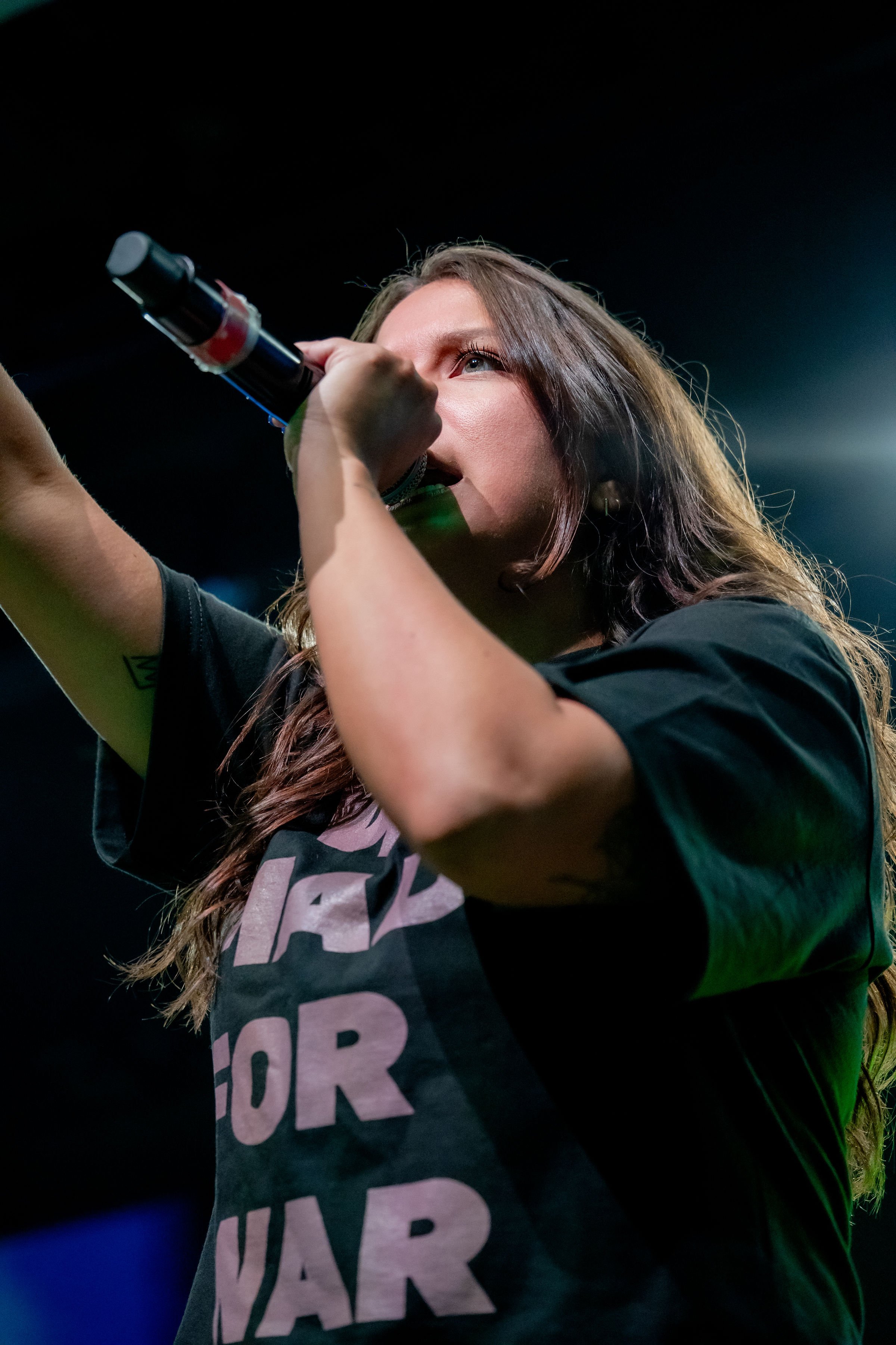 Female singer holding a microphone and performing on stage with dark background.