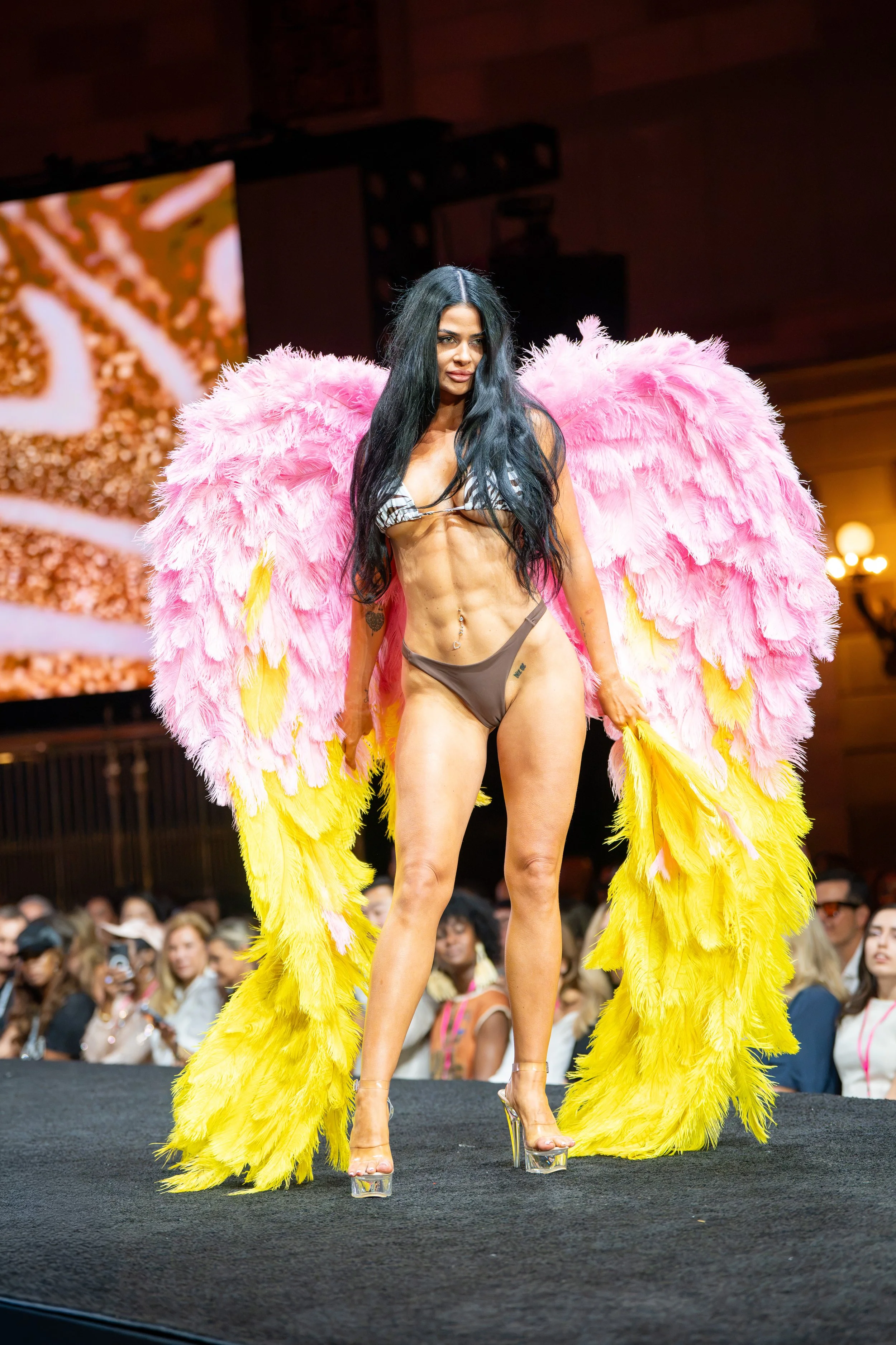 Runway model wearing dramatic pink and yellow feather wings during a Krissy King presentation at New York Fashion Week.