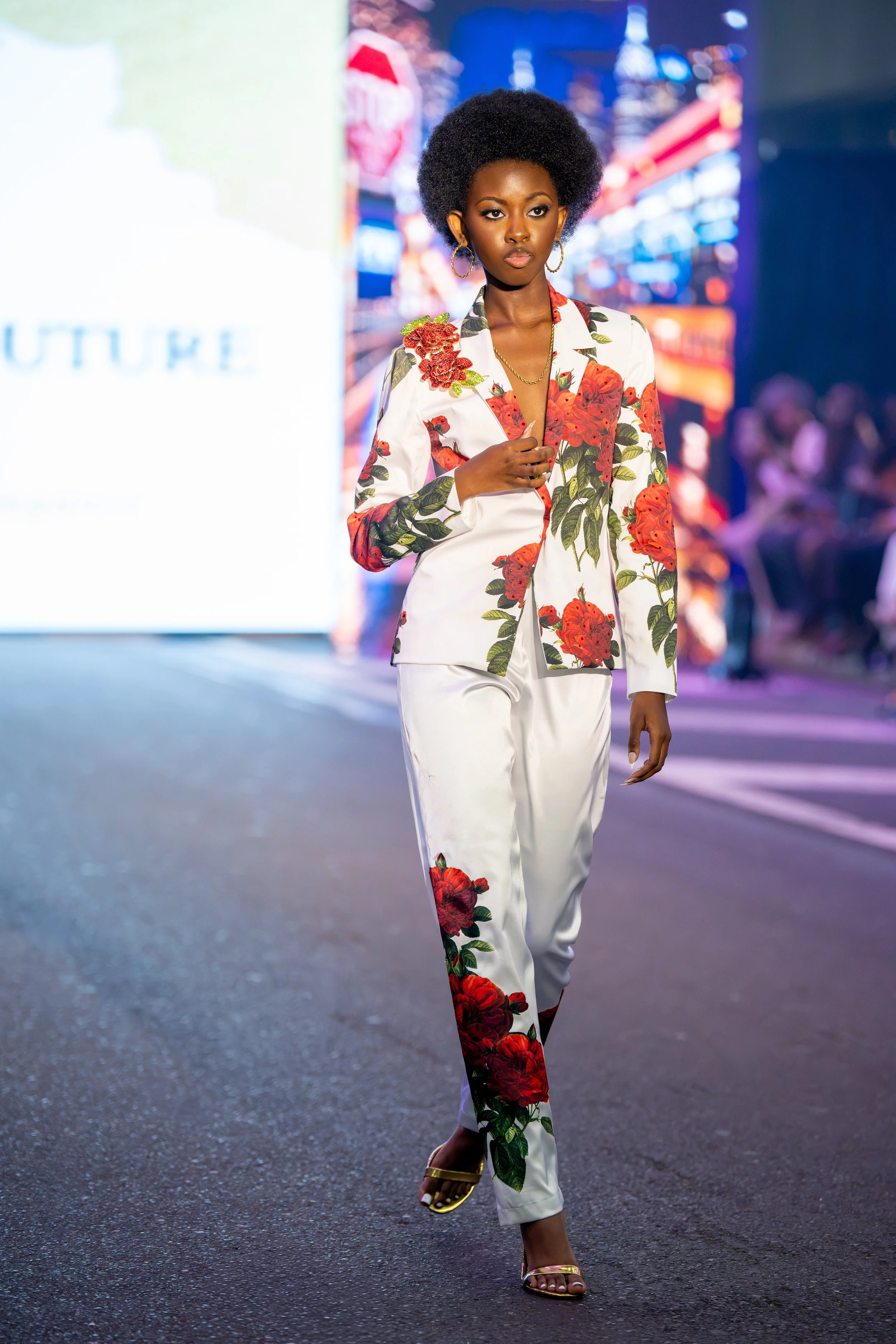 Model walking the Philly Fashion Week runway in a white tailored suit decorated with bold red floral detailing and matching floral accents along the pants.