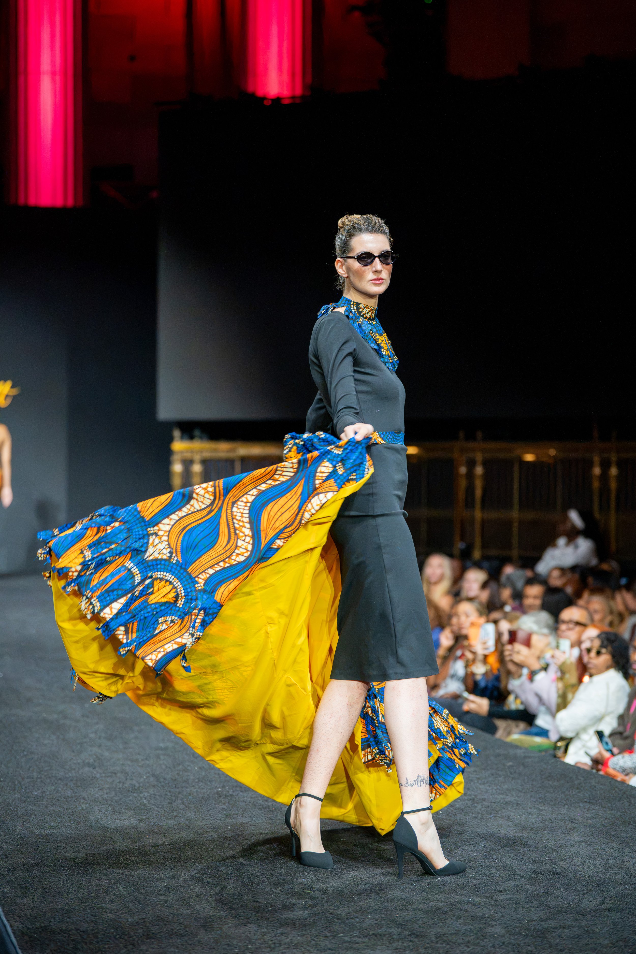 Model in a black runway look with dramatic blue and yellow fabric movement during New York Fashion Week at Gotham Hall.