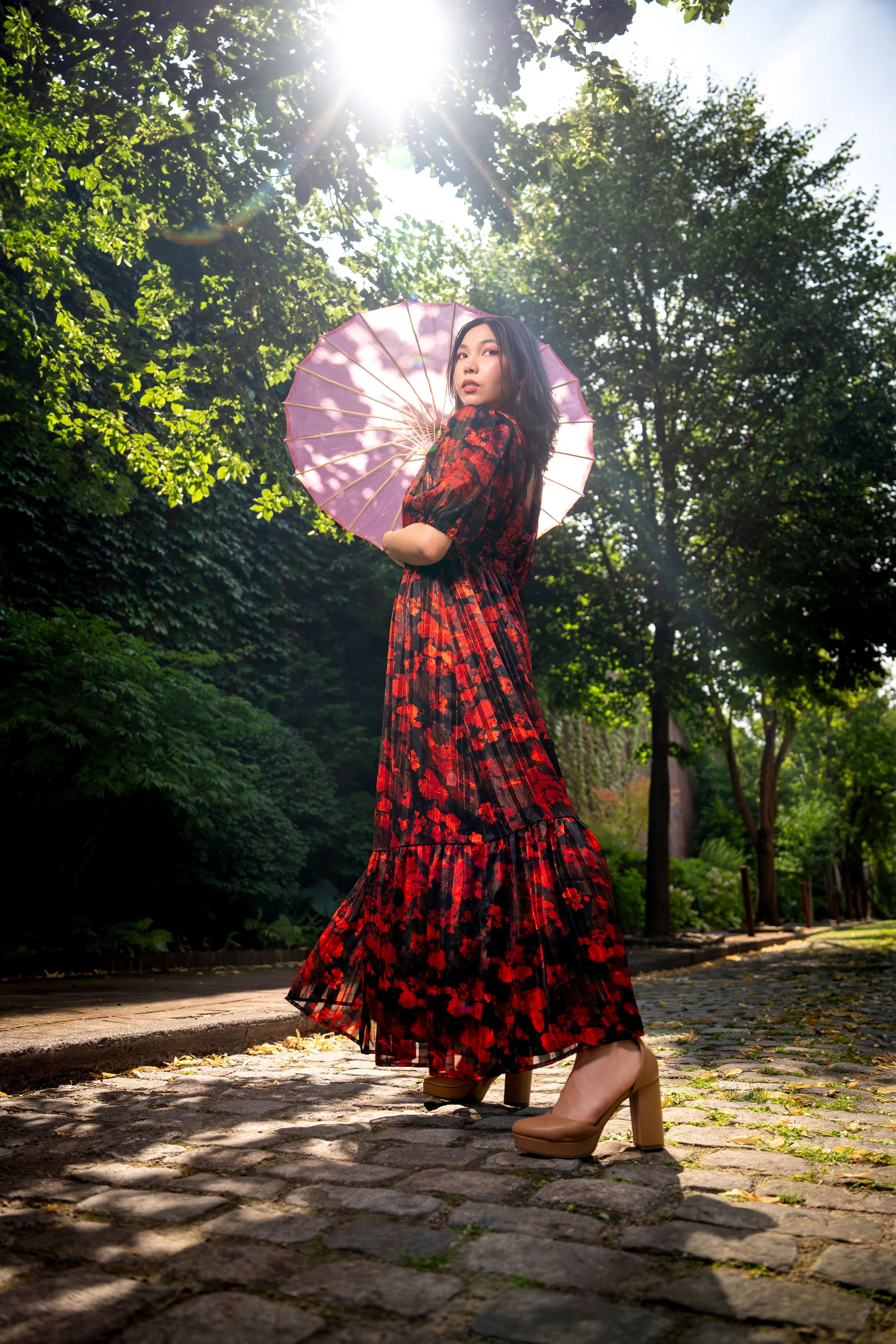 Editorial portrait of a model in a flowing floral dress photographed in a natural outdoor setting.