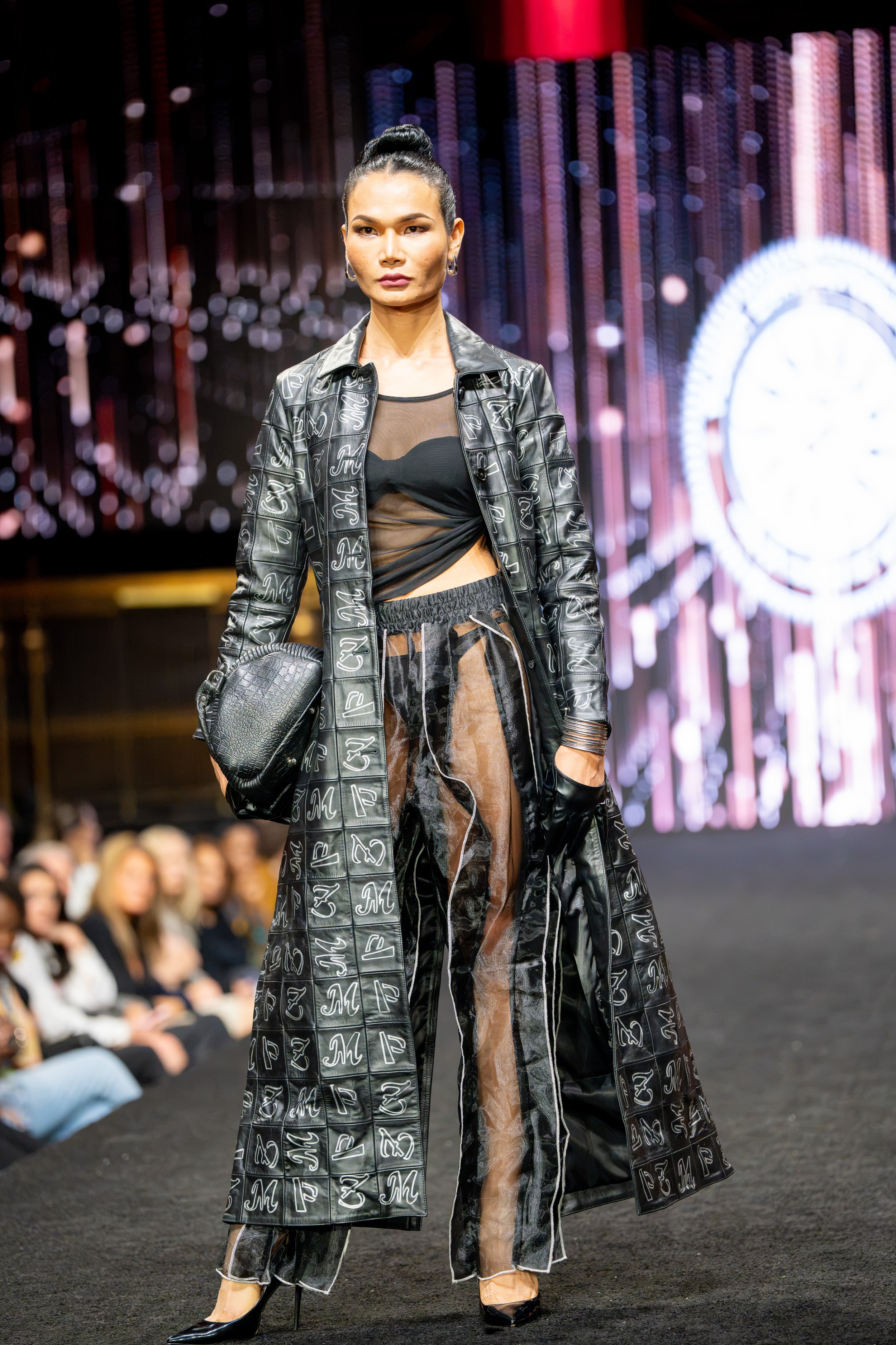 Model walking the runway in a long black leather fashion look during The Bureau Fashion Week presentation in New York City.