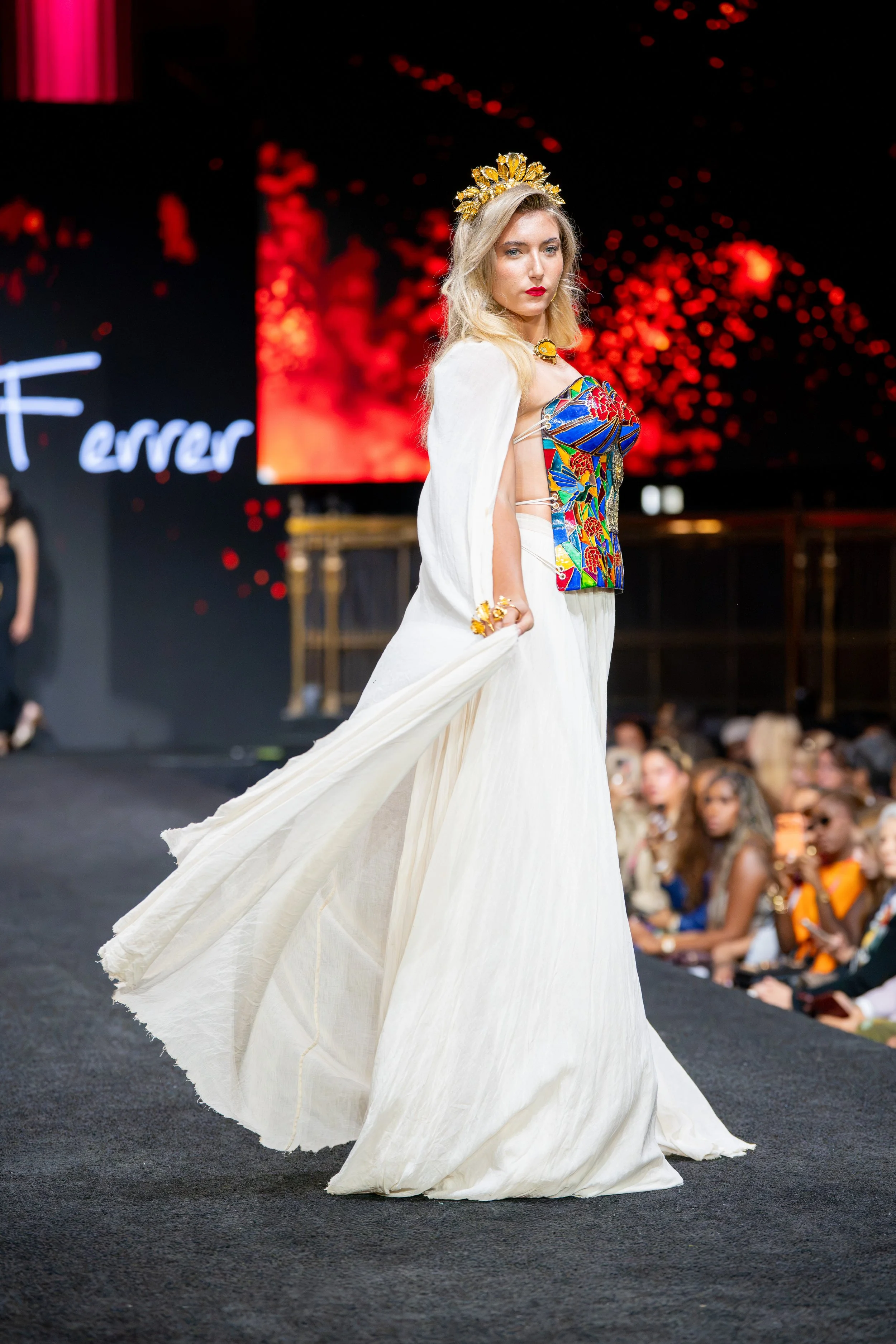 Model in a flowing white gown captured in motion against a dramatic red backdrop during New York Fashion Week at Gotham Hall.