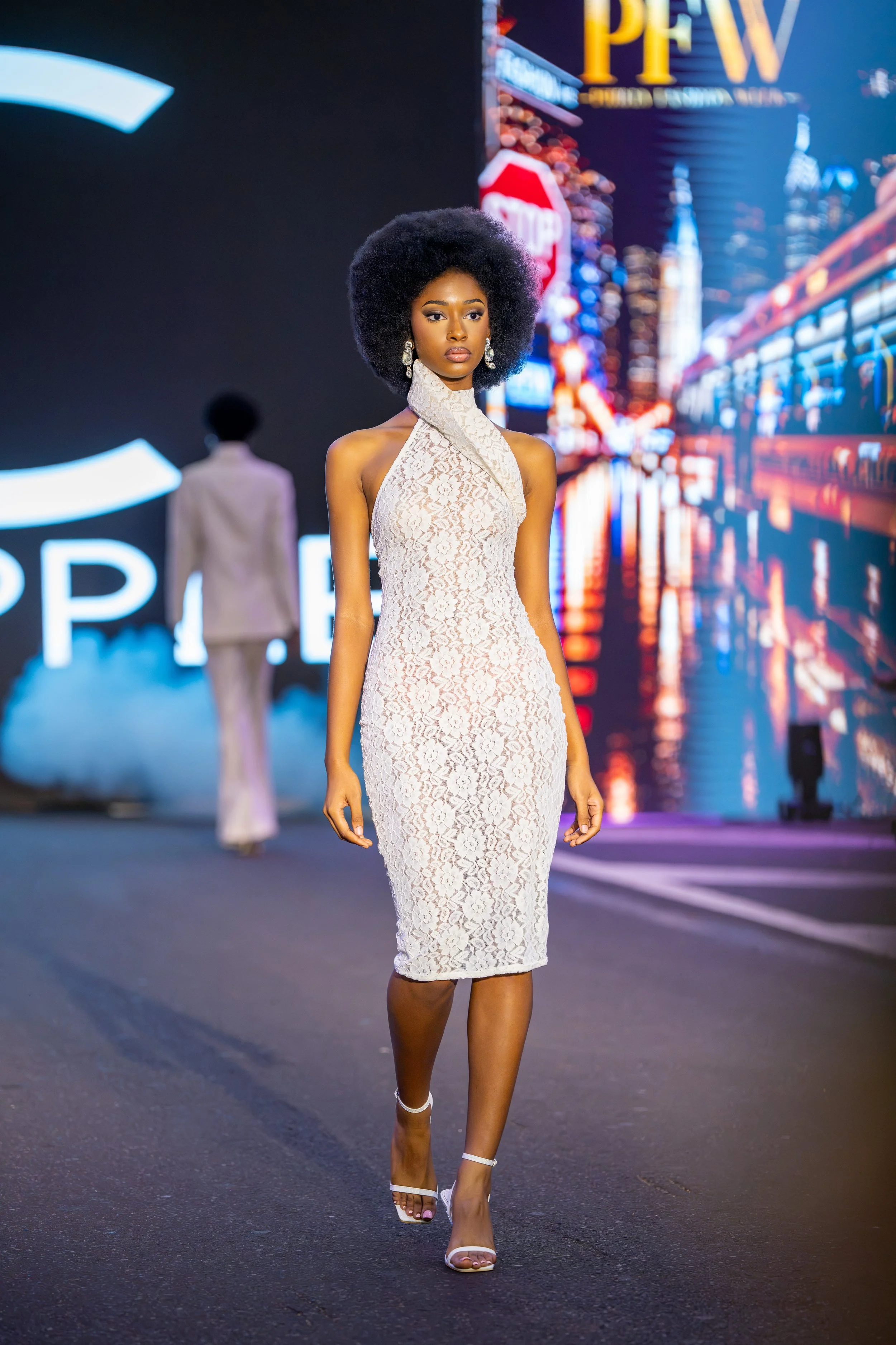 Model on the Philly Fashion Week runway wearing an elegant white lace halter dress with an asymmetrical neckline and fitted silhouette.