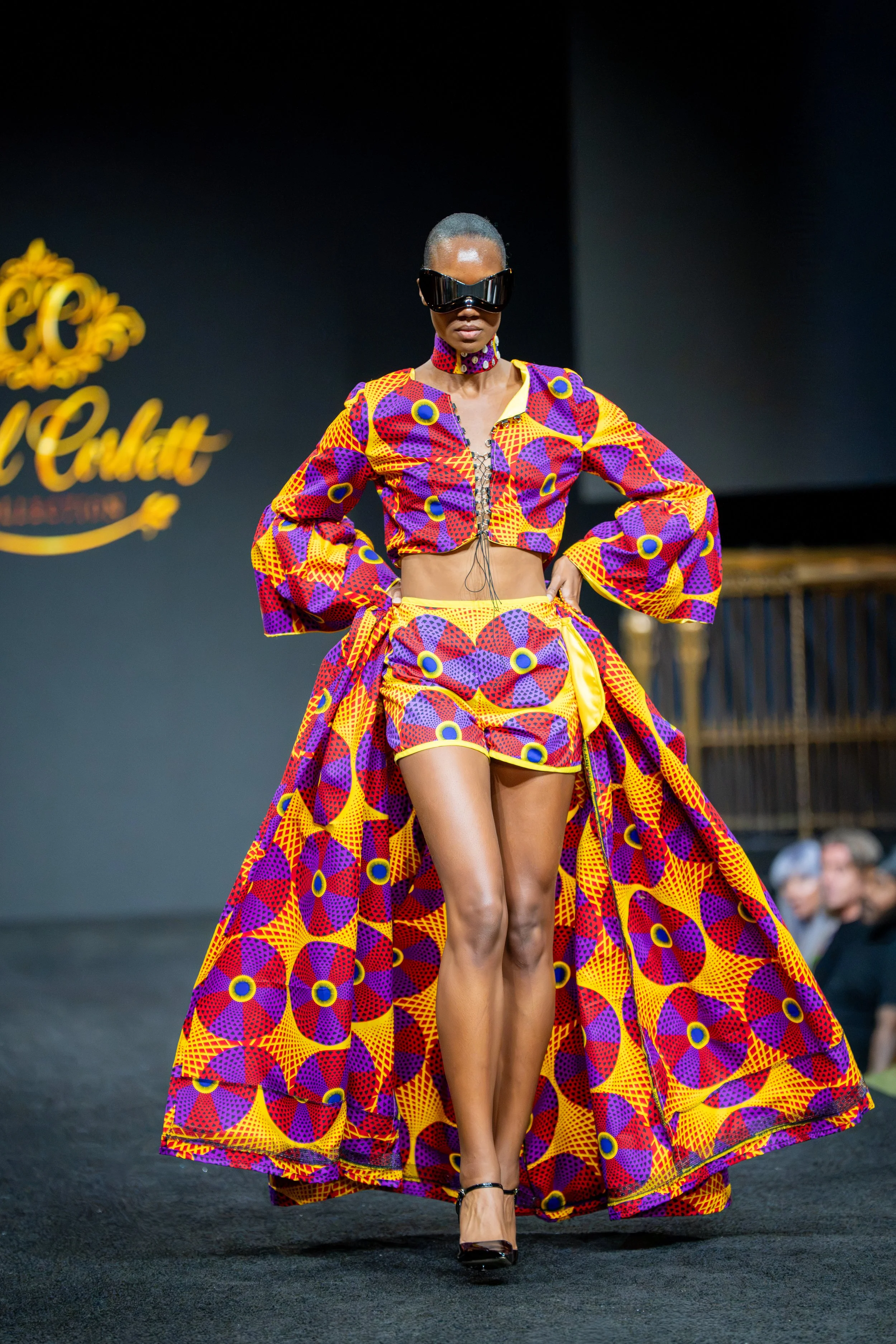 Model walking the runway in a vibrant purple, orange and yellow patterned fashion look during New York Fashion Week at Gotham Hall.