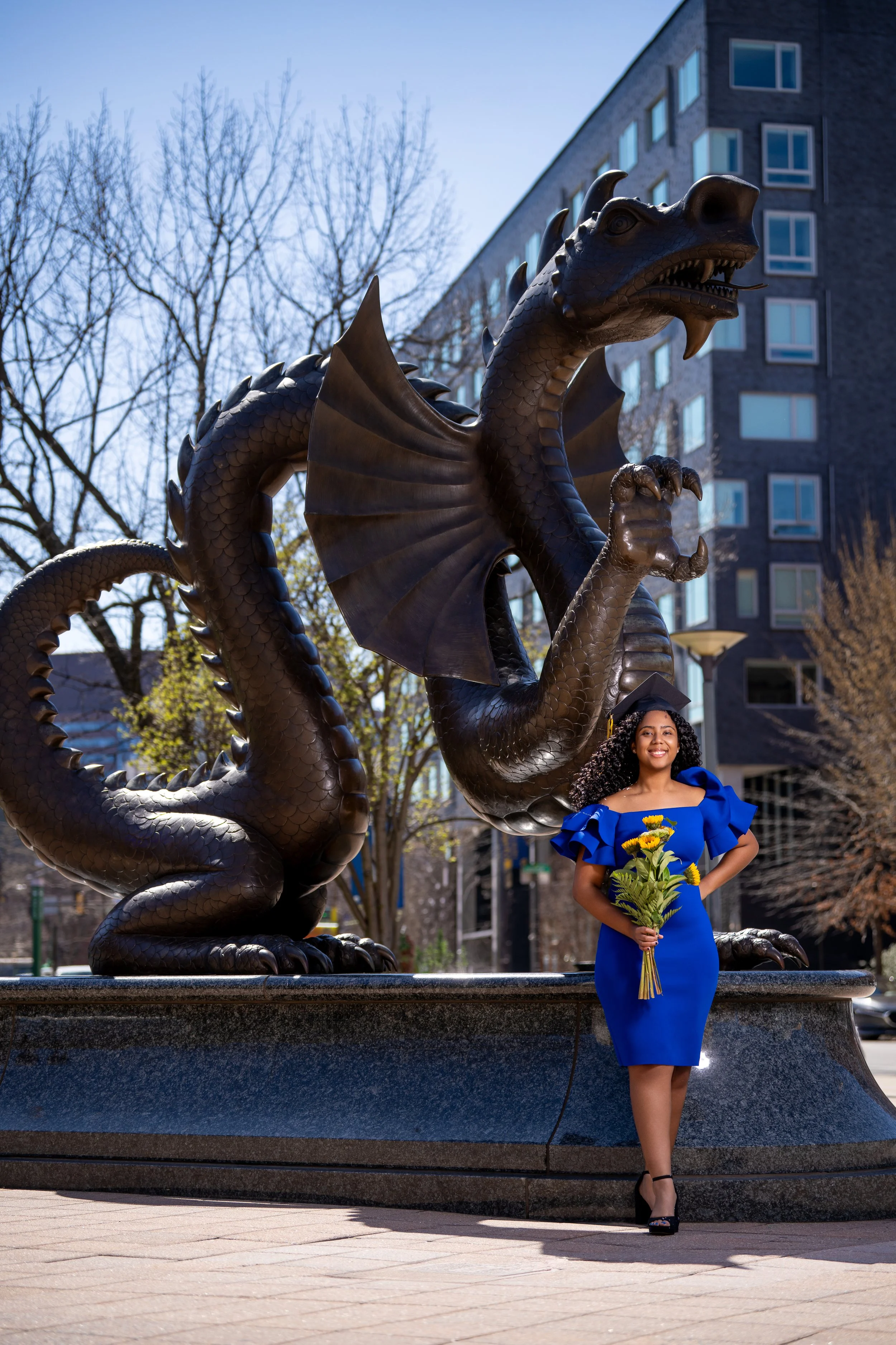 creative graduation photoshoot in Philadelphia featuring female graduate in blue dress posing near dragon statue