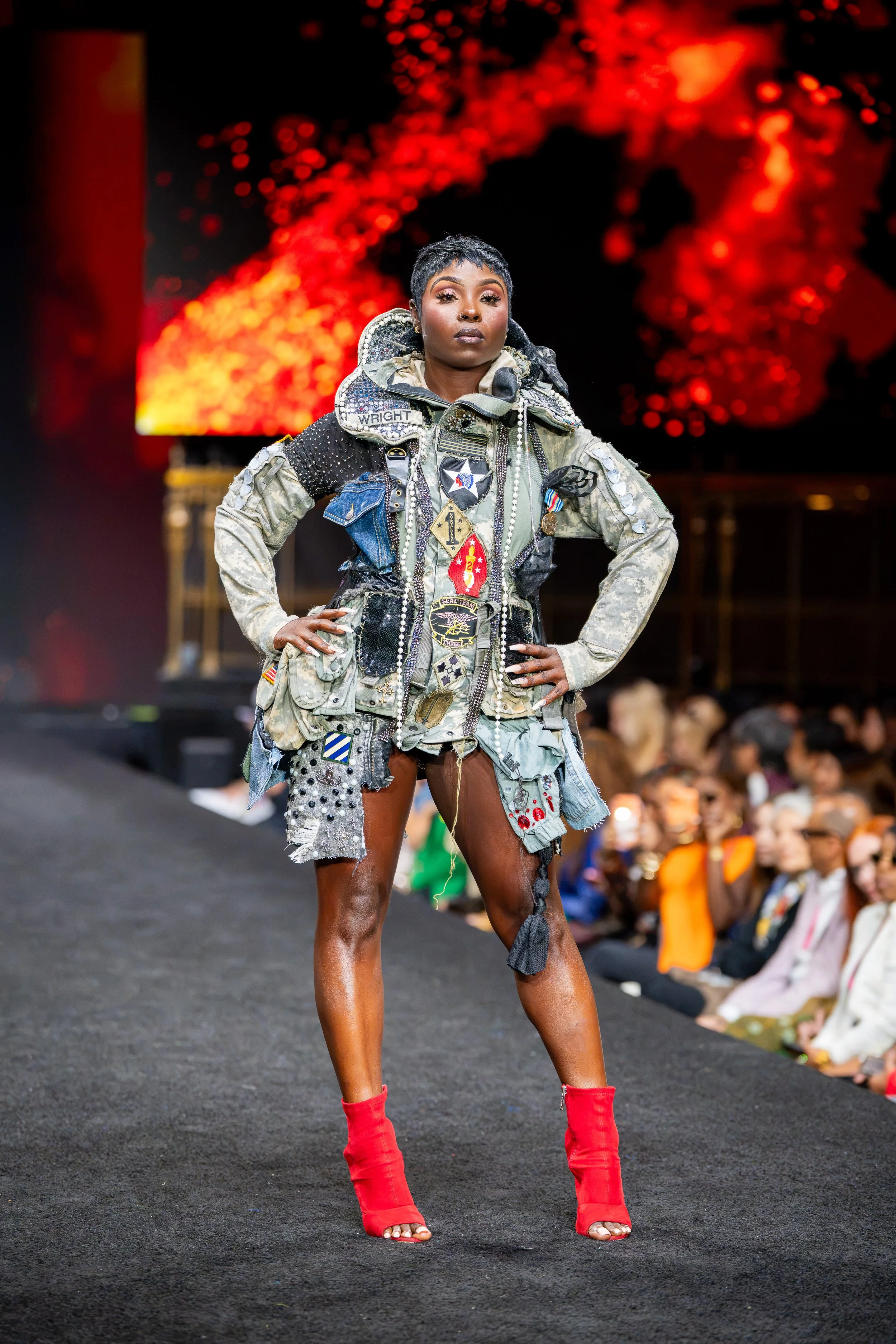 Model wearing a gray military-inspired patchwork look with bold red boots on the New York Fashion Week runway at Gotham Hall.