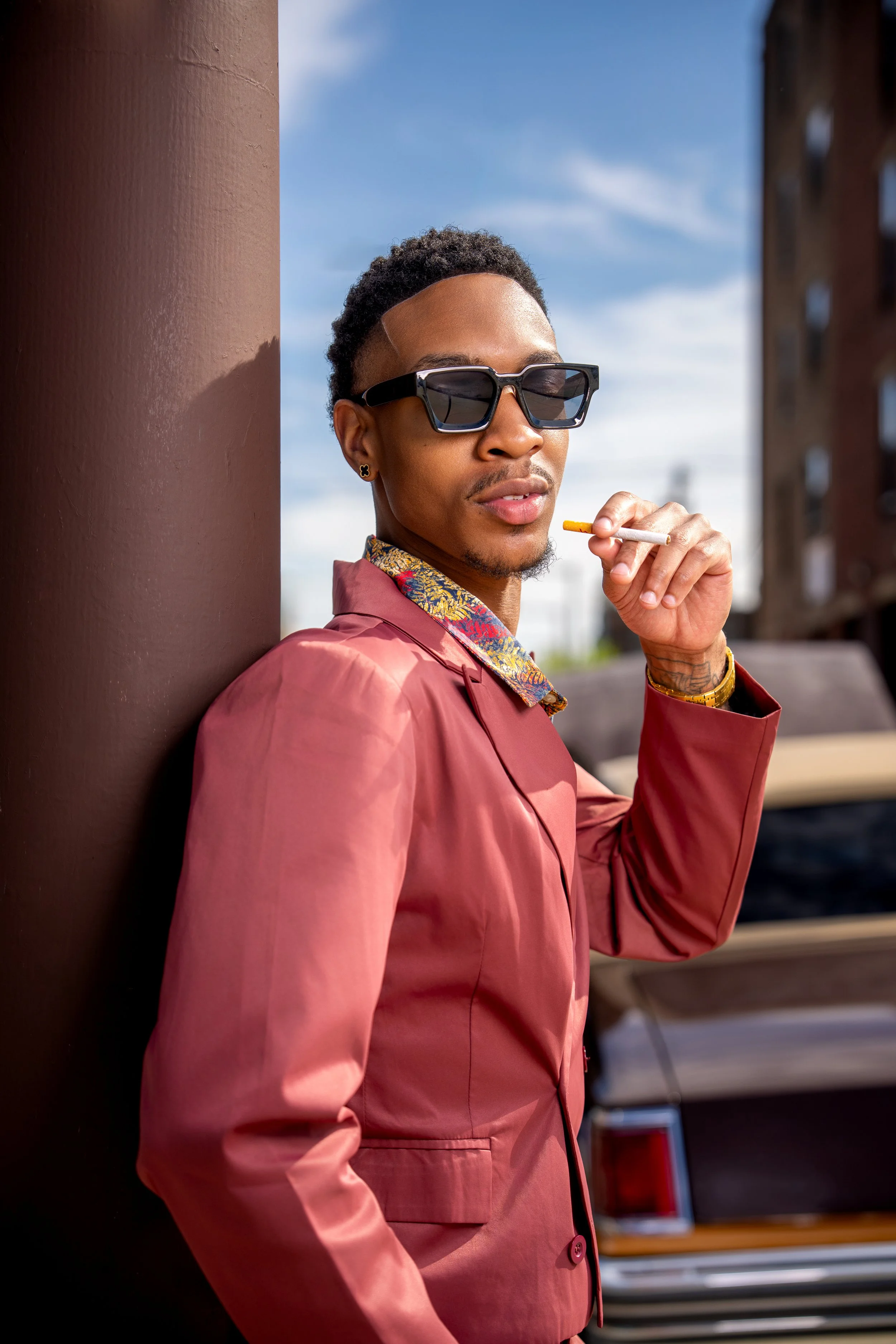 Editorial portrait of a male fashion model wearing sunglasses in an urban environment.
