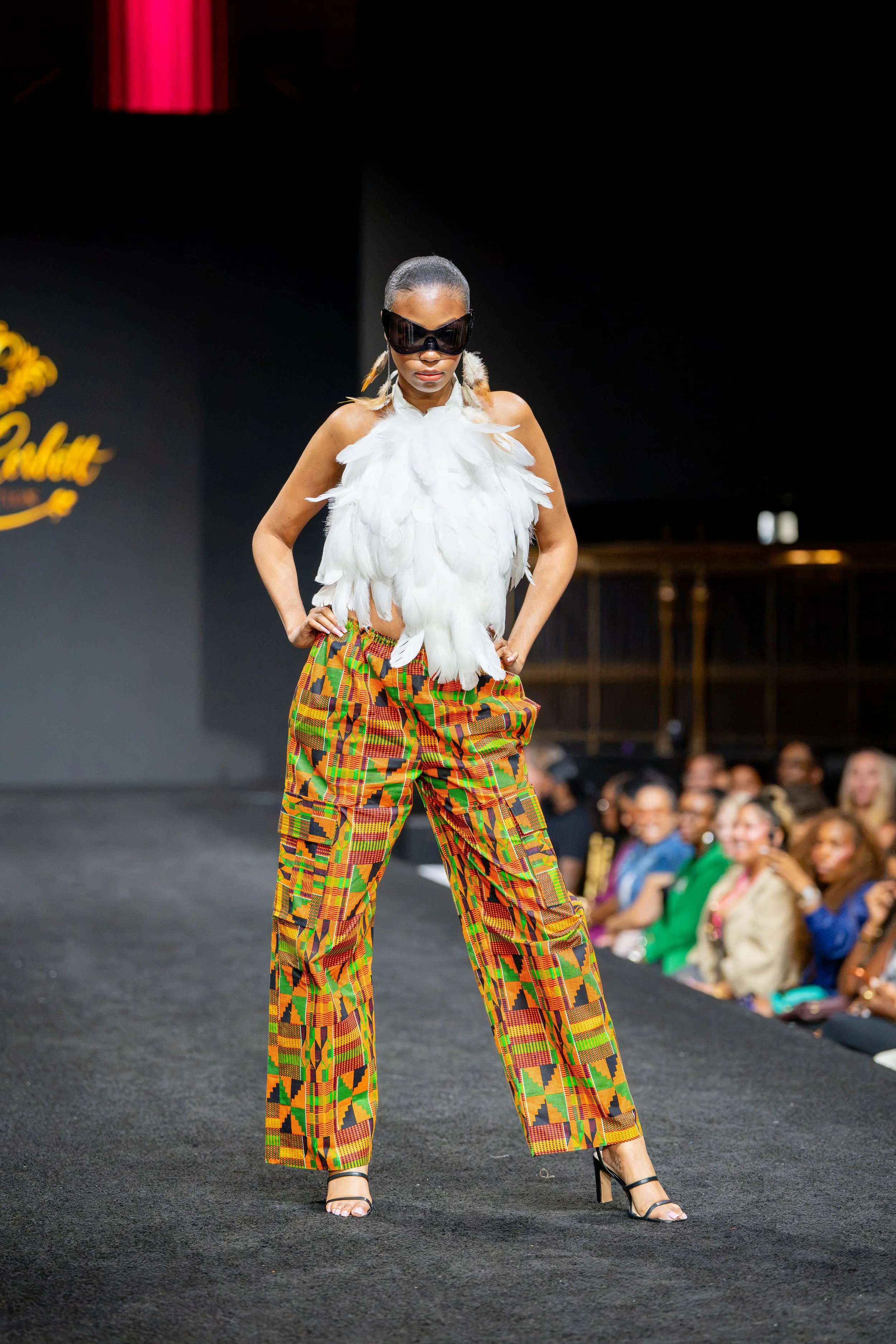 Model in a white feathered top, colorful patterned pants and sunglasses walking the runway during New York Fashion Week at Gotham Hall.