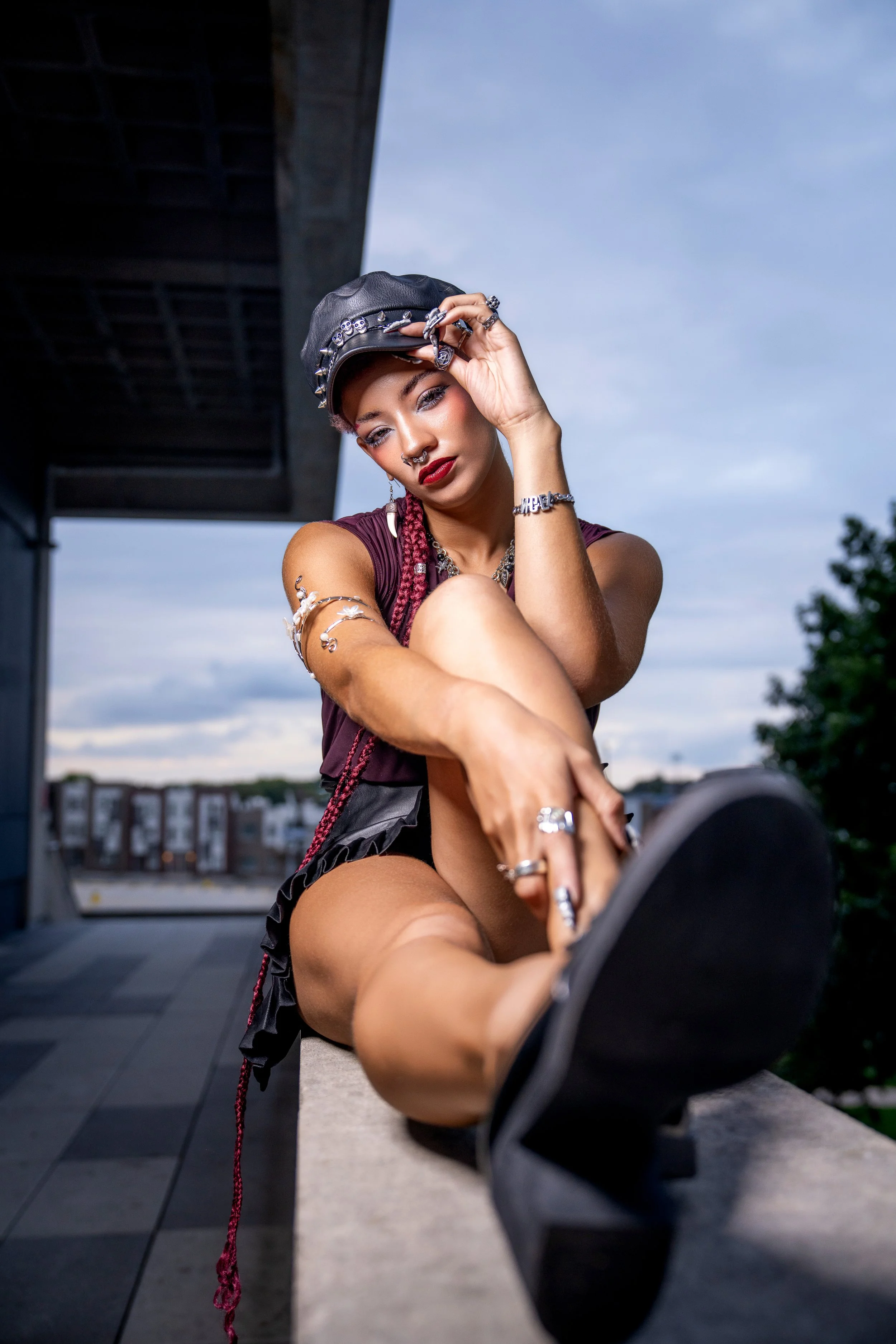 Bold editorial fashion portrait featuring a seated model in a leather-inspired look, photographed from a dramatic low angle with strong perspective and confident styling.