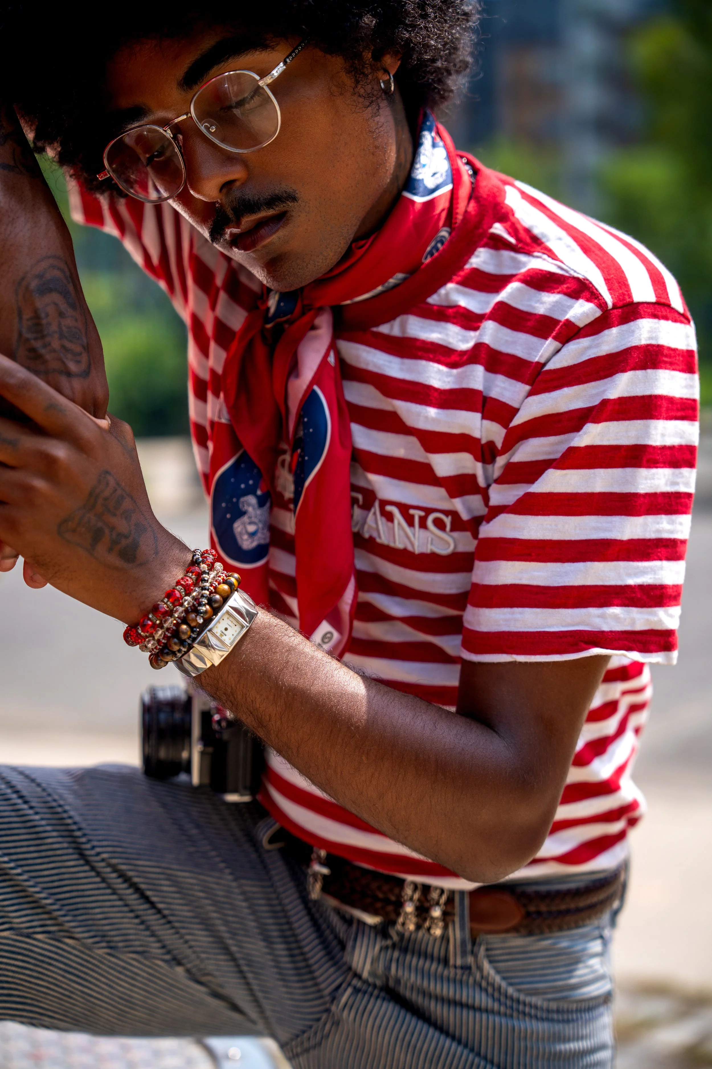 Close-up editorial portrait of a male model wearing a red and white striped shirt, vintage glasses, layered jewelry and a red neck scarf.