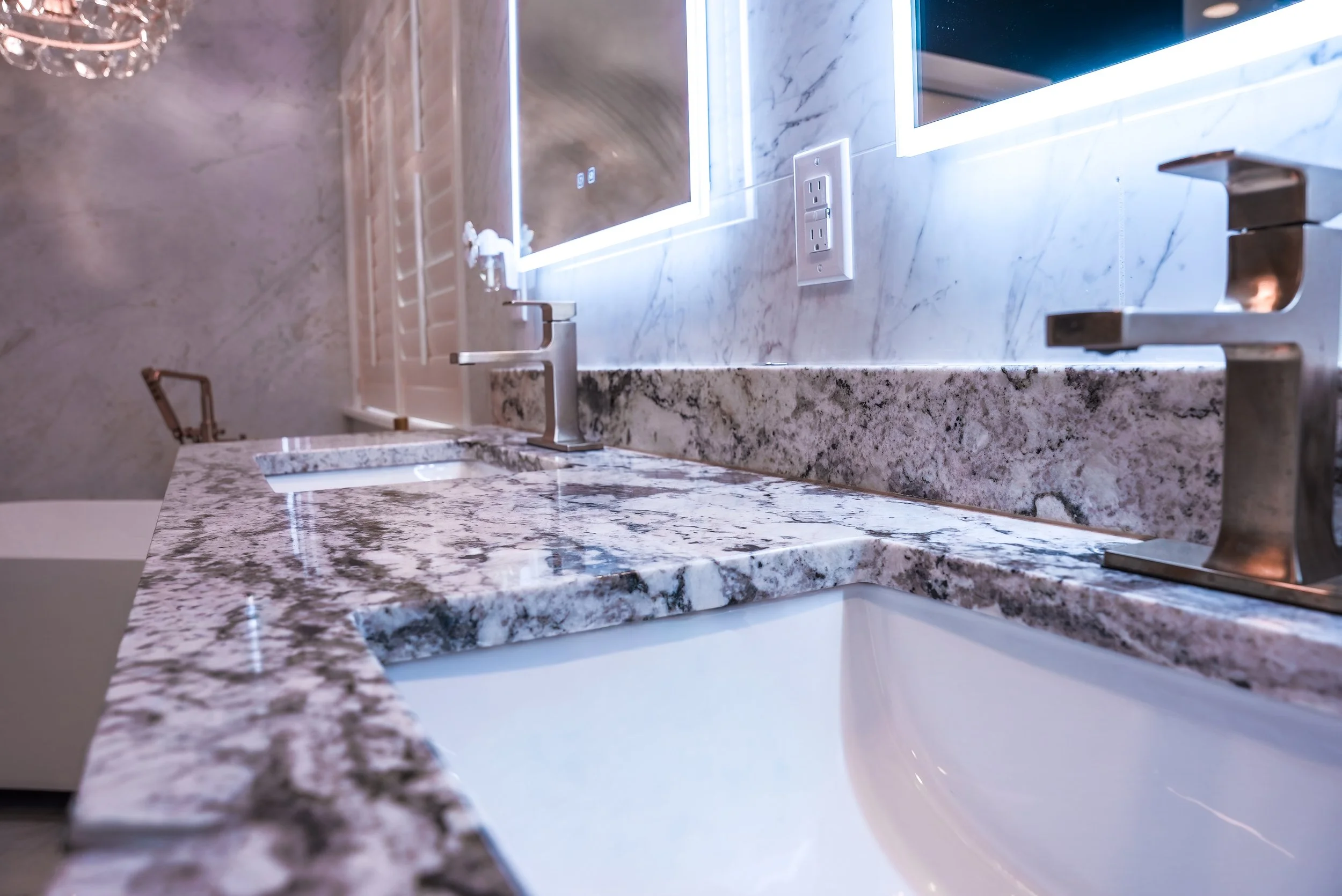 Close-up of a marble bathroom countertop with a sink, faucet, and a mirror with LED lighting.