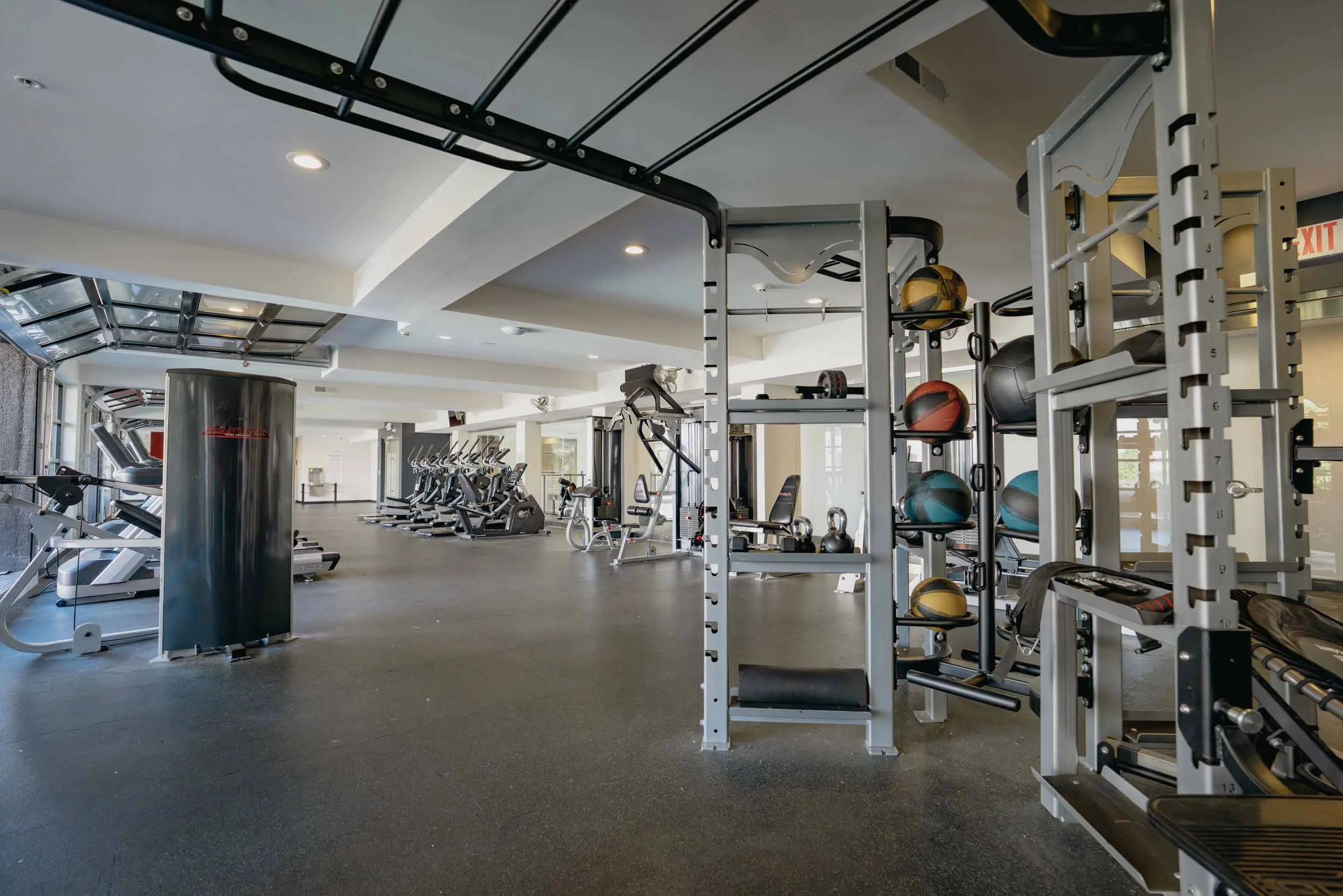 A spacious gym with fitness equipment, including treadmills, exercise bikes, weight racks with kettlebells and medicine balls, under a ceiling with circular recessed lighting.
