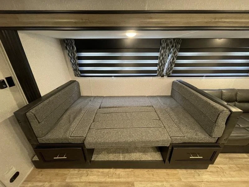 A sofa bed in a living room with patterned window blinds and wooden flooring.