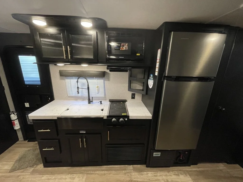 Interior of a small kitchen with black cabinets, a stainless steel refrigerator, a white countertop with a sink, and a microwave.