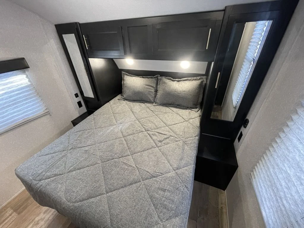 Small bedroom with a bed, black cabinetry, gray pillows, and a window with blinds.