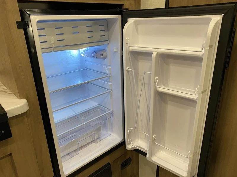 Open compact refrigerator showing empty interior with shelves and light, situated in a wooden cabinet.