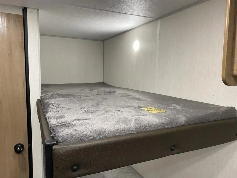 A small, cozy sleeping area with a bed covered with a gray plush blanket inside a cabin or RV.