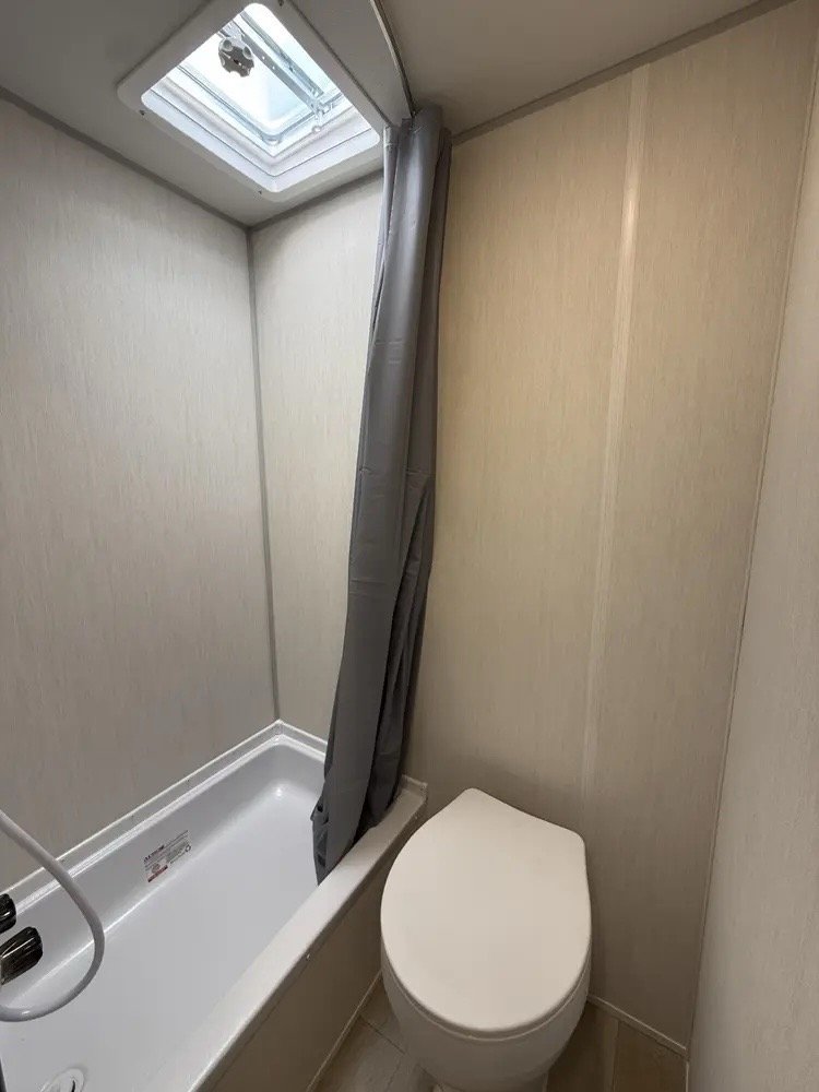 Small bathroom with a bathtub and toilet next to each other, a gray shower curtain partially drawn, and a skylight window on the ceiling.