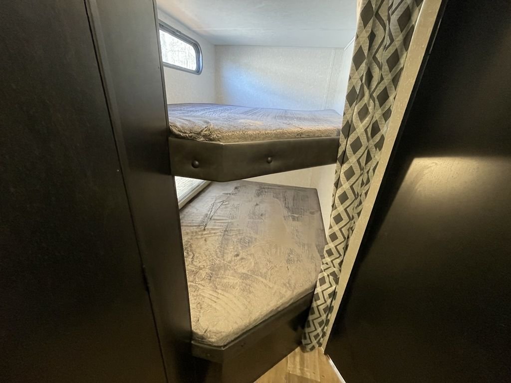 Bunk beds with mattresses in a small room with a window and patterned curtain.