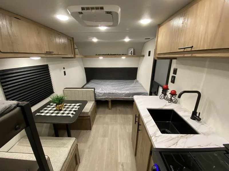 Interior of an RV with a small kitchen, a dinette, and a bed in the background.
