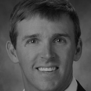 Black and white portrait of a young man with short hair, smiling, wearing a suit and tie.