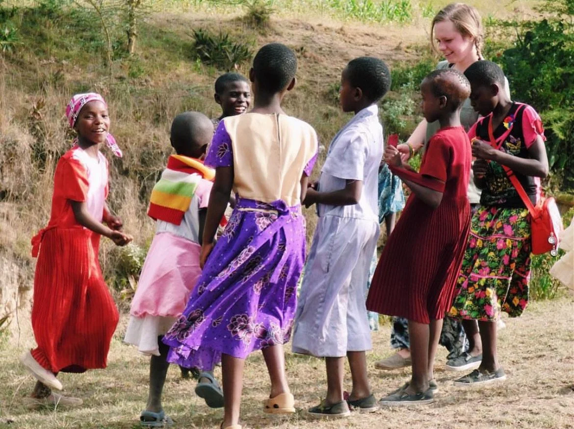 Children dressed in colorful traditional clothing playing outdoors on grassy terrain.