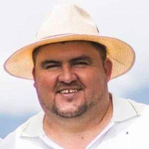 Man wearing a wide-brimmed straw hat and white shirt, smiling outdoors.