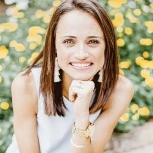 A young woman smiling outdoors with yellow flowers in the background