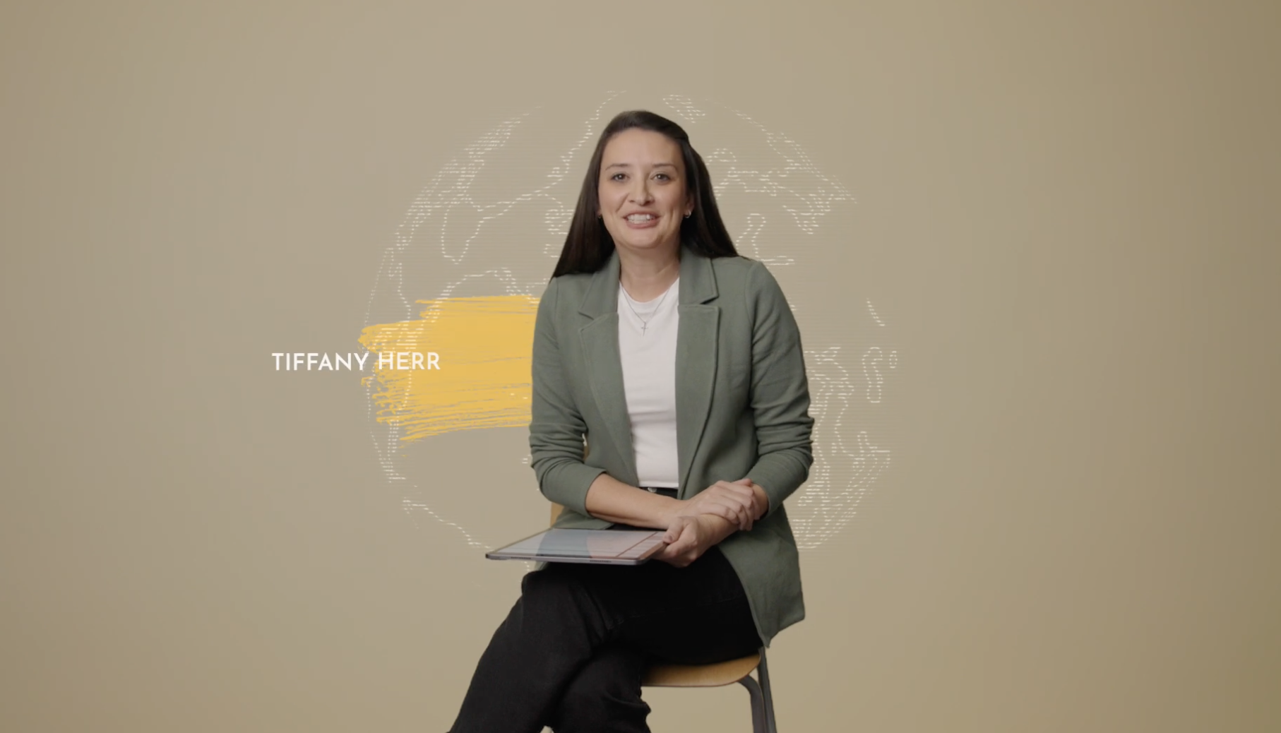 A woman with long dark hair sitting on a chair, holding a tablet, wearing a grey blazer and black pants, with a light beige background and digital graphics of a world map. Text displaying the name Tiffany Herr appears next to her.
