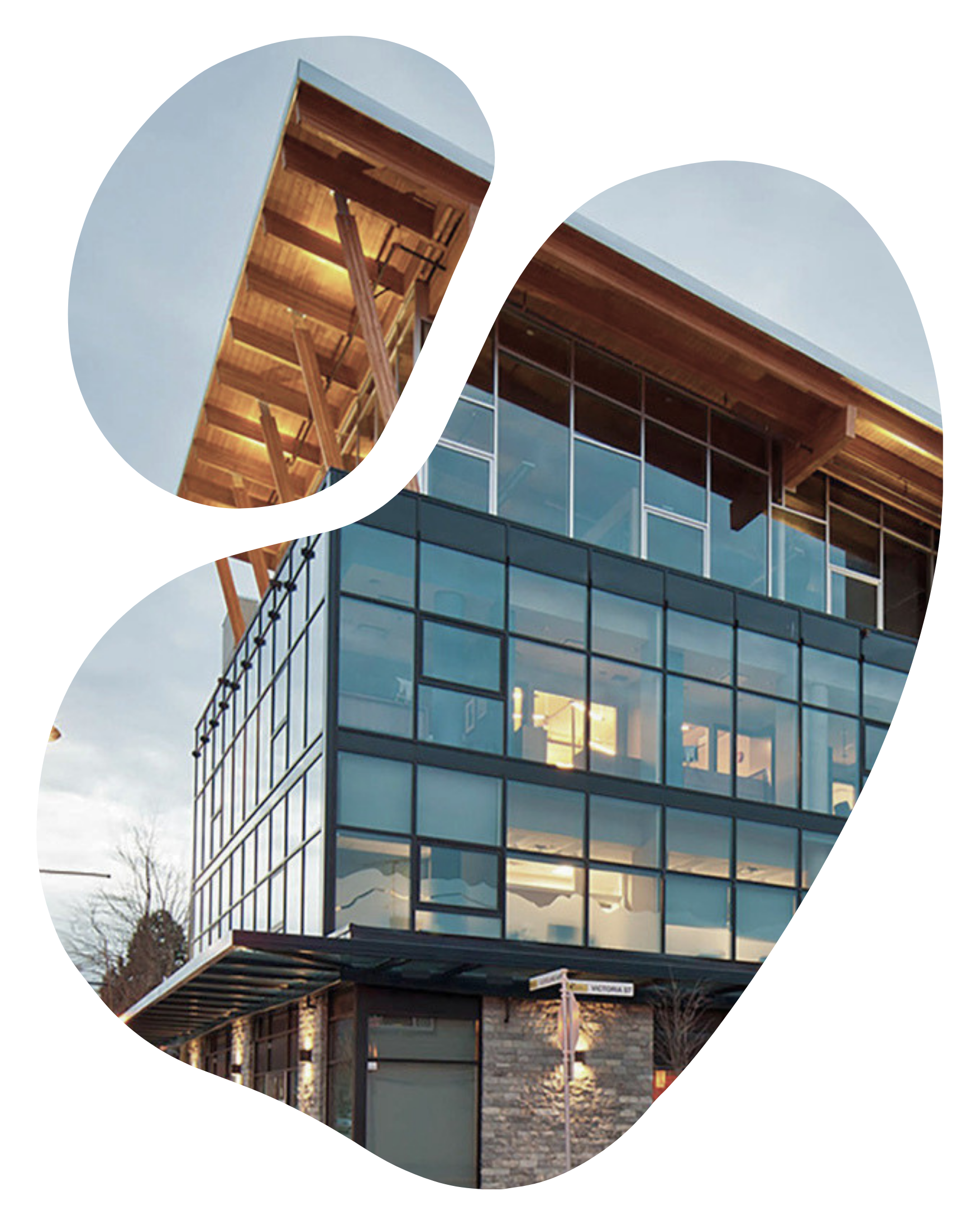 Modern multi-story building with large glass windows and a stone facade, featuring an exposed wooden ceiling structure on the top floor.