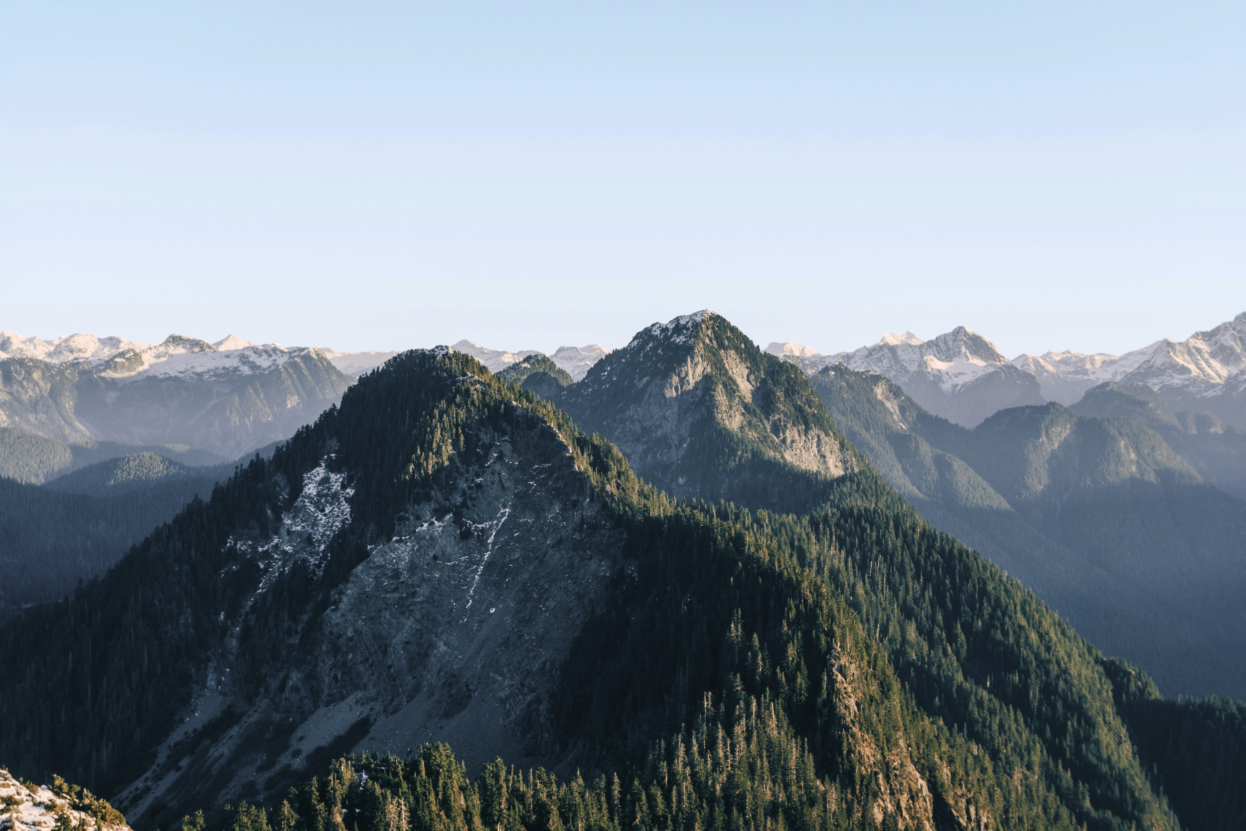 Mountain range with green forested slopes and snow-capped peaks in the distance during daylight.