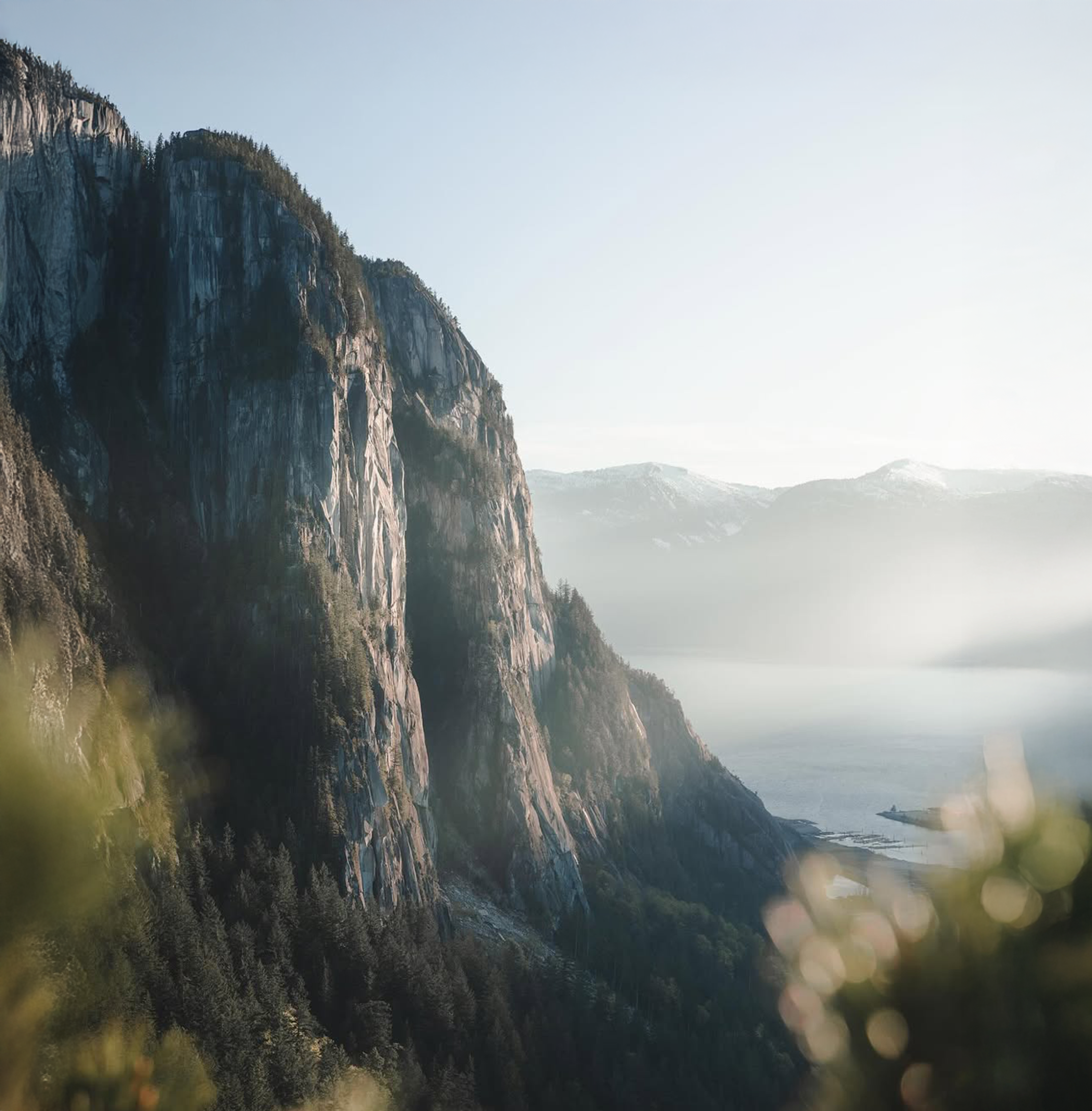 Landscape of a mountain with cliffs overlooking a lake, with distant mountains, under a bright sky.