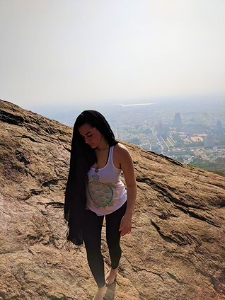 Woman standing on rocky hilltop with cityscape in the background, wearing a tank top and leggings.