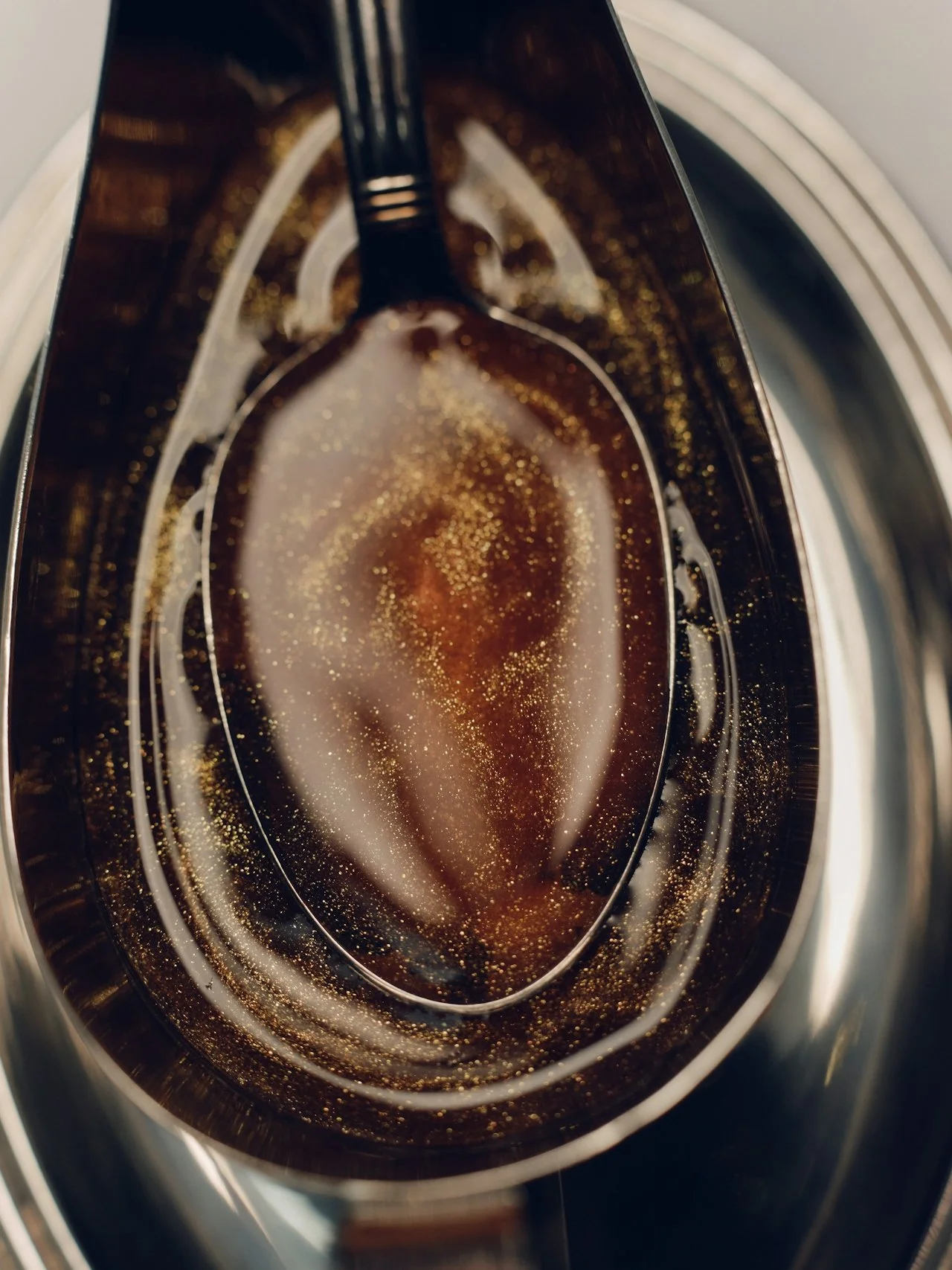 Close-up view of a spoon immersed in a dark, carbonated beverage with bubbles, inside a metallic container.