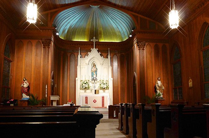 Interior of a church with wooden walls, pews, an altar with a statue, and a domed ceiling.