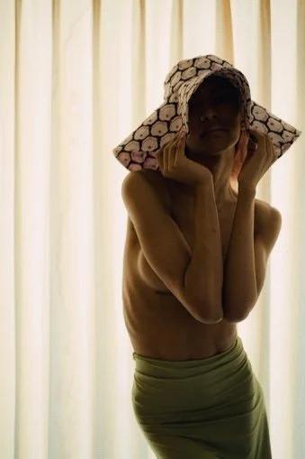 Person holding a bundle of rolled papers over their head, standing in front of light-colored curtains.
