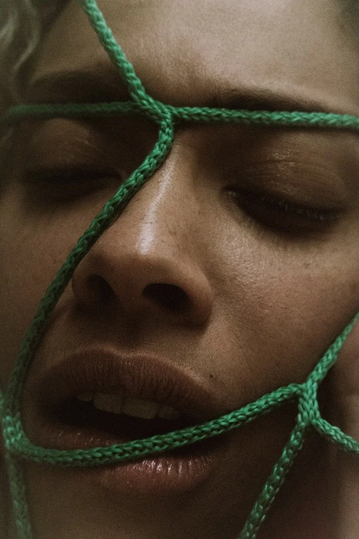 Close-up of a person's face with eyes closed, lips slightly parted, and green rope arranged across their face.