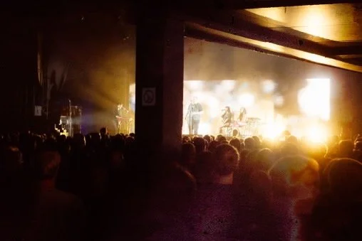 A concert with a large crowd seated and facing a brightly lit stage with performers.