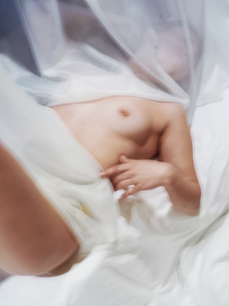 A person lying in bed, partially covered with a blanket, with visible part of their upper body and abdomen.