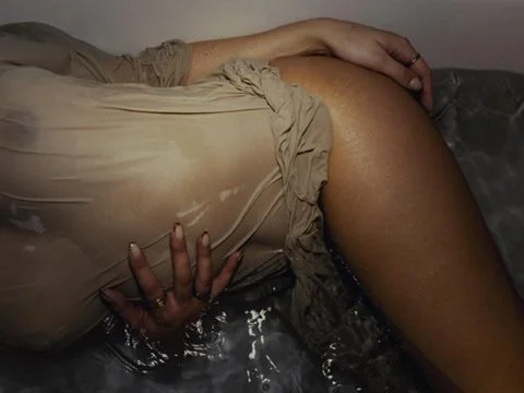 A person lying sideways with a beige dress and their hand resting on their thigh, in water.