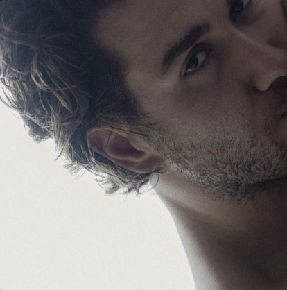 Close-up of a young man's face and shoulder with a light background.