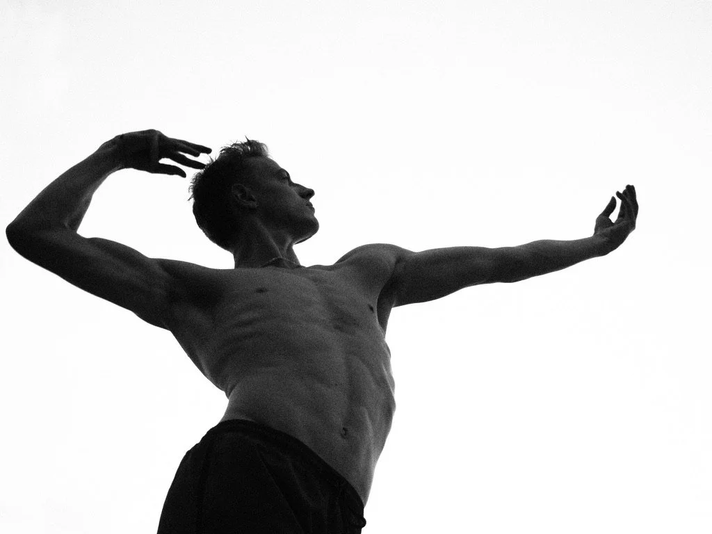 Silhouette of a shirtless man with a muscular build, standing against a plain background, striking a pose with one arm extended and the other hand near his head.