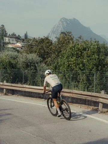 Person riding a bicycle on a road with trees and mountains in the background.