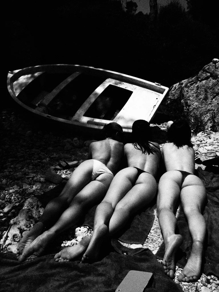 Three women lying on a beach at night, facing away from the camera, with an overturned boat nearby.
