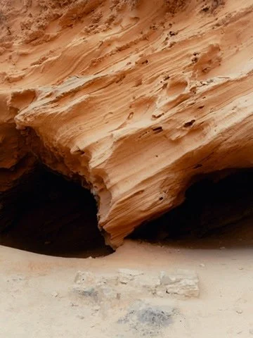 Close-up of a desert rock formation with layered, weathered sandstone and a dark cave opening