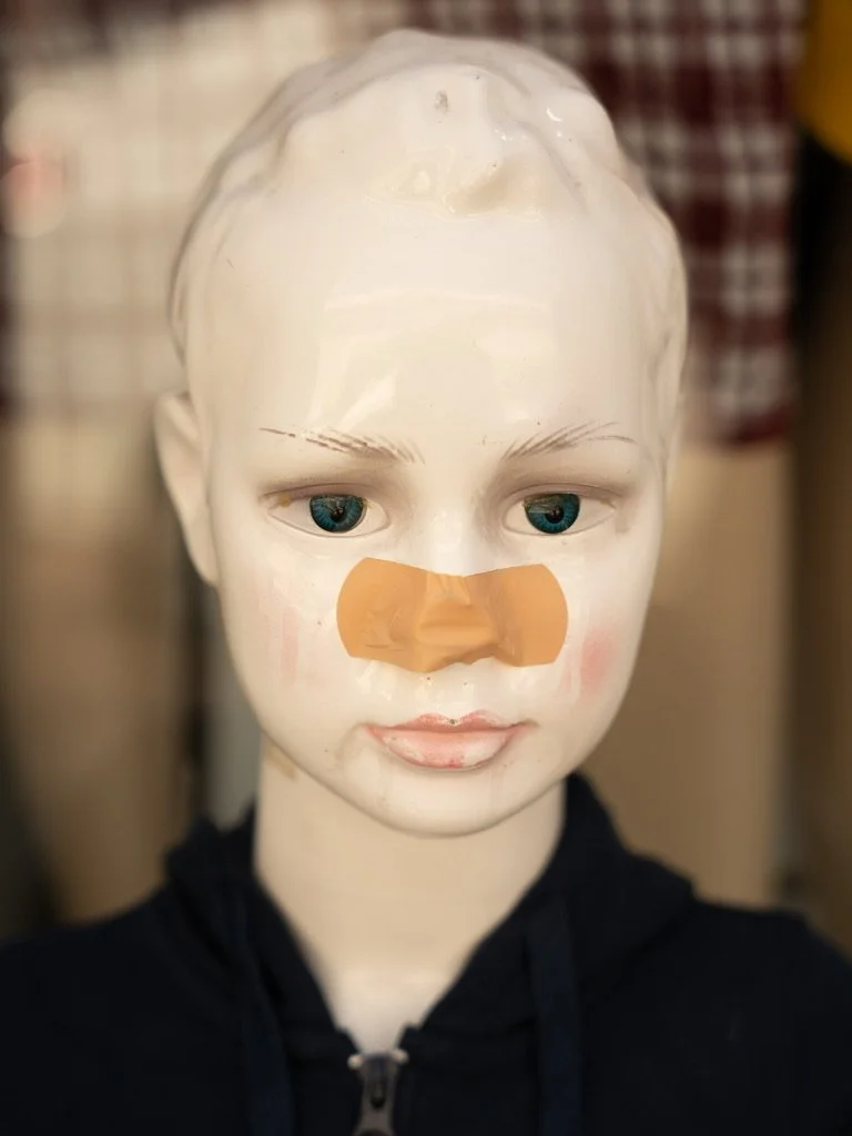 A mannequin head with a bandage on its nose, wearing a black hoodie, in a setting that appears to be a store or workshop.