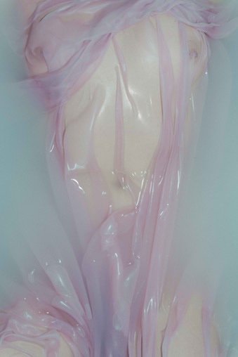 A person covered in pink and translucent plastic in a bathtub filled with water.